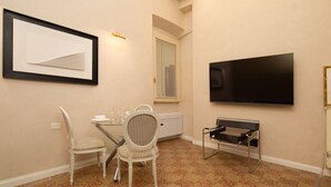 Ein Zimmer mit Esstisch, Stühlen, einem Flachbildfernseher und einem gerahmten Kunstwerk an der Wand.