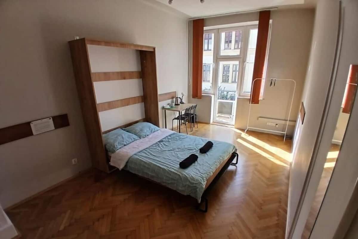 A bedroom with a bed, wooden headboard, a desk with a chair, and a window with curtains.