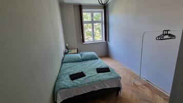 Un dormitorio con cama, ventana, lámpara colgante y perchero.