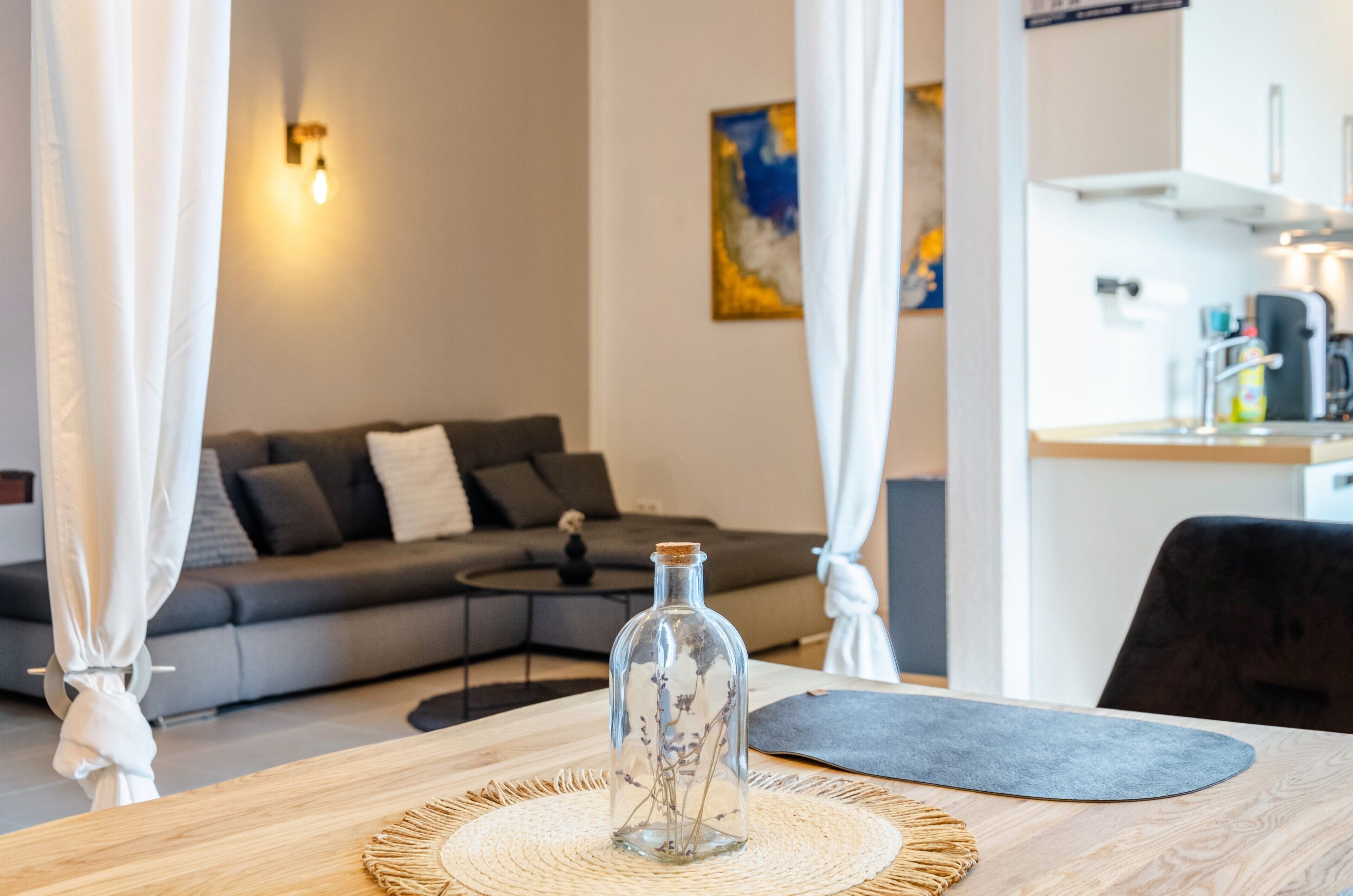 Ein Wohnzimmer mit einer Couch, einer Glasflasche auf einem Tisch und einer Küchenzeile im Hintergrund.