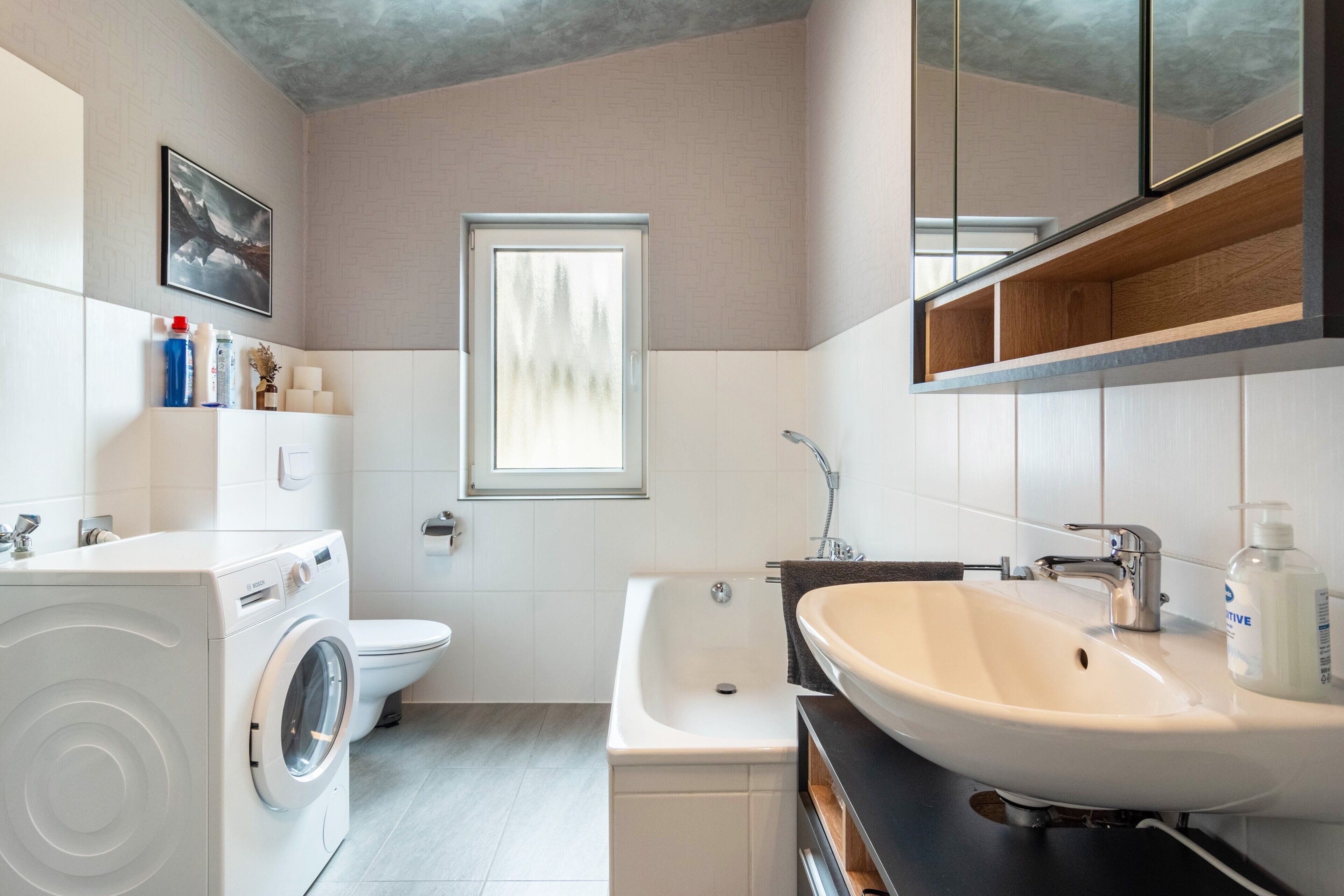 A modern bathroom with a washing machine, toilet, bathtub, and sink.