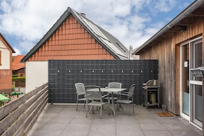 A patio with a table and chairs, a black fence, and a building with a sloped roof.