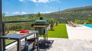 Un patio con una parrilla, una piscina y vistas a un paisaje montañoso.