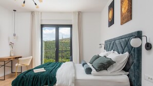 Un dormitorio con cama, escritorio, silla y vistas a la vegetación exterior.