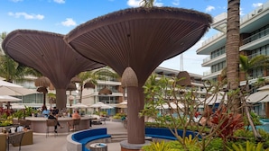 An outdoor lounge area with seating and umbrellas, surrounded by greenery and a pool. - Beachfront 1bedroom Apartment (Choeng Thale)