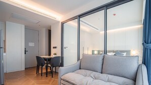 Ein modernes Wohnzimmer mit einem grauen Sofa, einem Esstisch mit Stühlen und einem großen Fenster mit Jalousien.