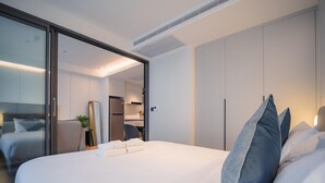 Ein modernes Hotelzimmer mit einem großen Bett, einer Schiebetür zu einer Küche und einem separaten Sitzbereich.