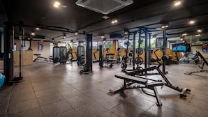 Ein Fitnessstudio mit unterschiedlichen Trainingsgeräten, einer digitalen Uhr und einem Fernseher, der ein Boxkampf übertragen zeigt.