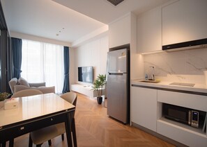 A modern kitchen with a built-in microwave, a refrigerator, and a dining area with a table and chairs. - Beachfront 189/240 One Bedroom Apartment (Choeng Thale)