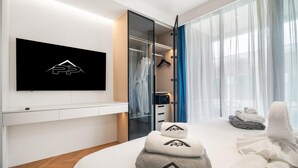 Een moderne hotelkamer met een flatscreen televisie aan de muur, een inloopkast met spiegel, en een bed met netjes opgevouwen handdoeken en badjassen.