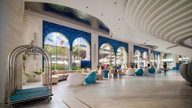 Een ruime lobby met een modern design, met een grote zithoek, een servicewagen en uitzicht op het buitengebied door grote ramen.