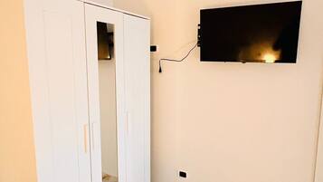 Ein Zimmer mit weißem Kleiderschrank, einem flachbildfernseher an der Wand und einem Boden mit Marmoroptik.