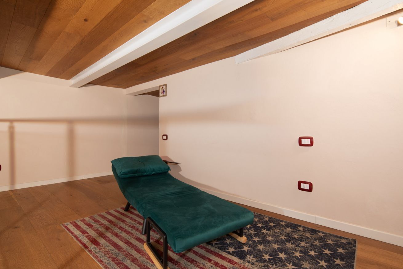 A small, single-bed room with a wooden ceiling, a teal bedspread, and a patterned rug.
