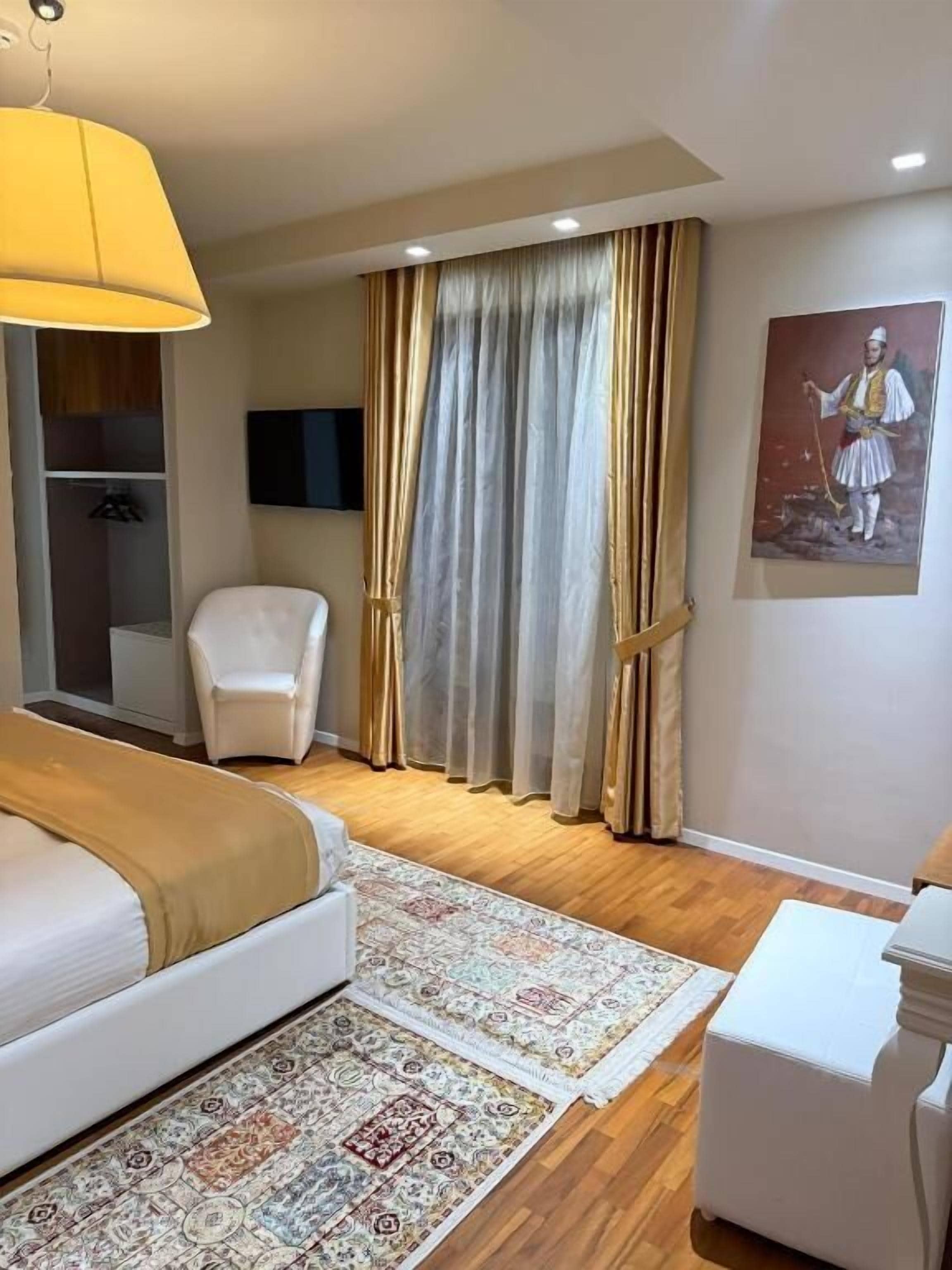 A hotel room with a bed, a chair, a desk, a television, and a large window with curtains.