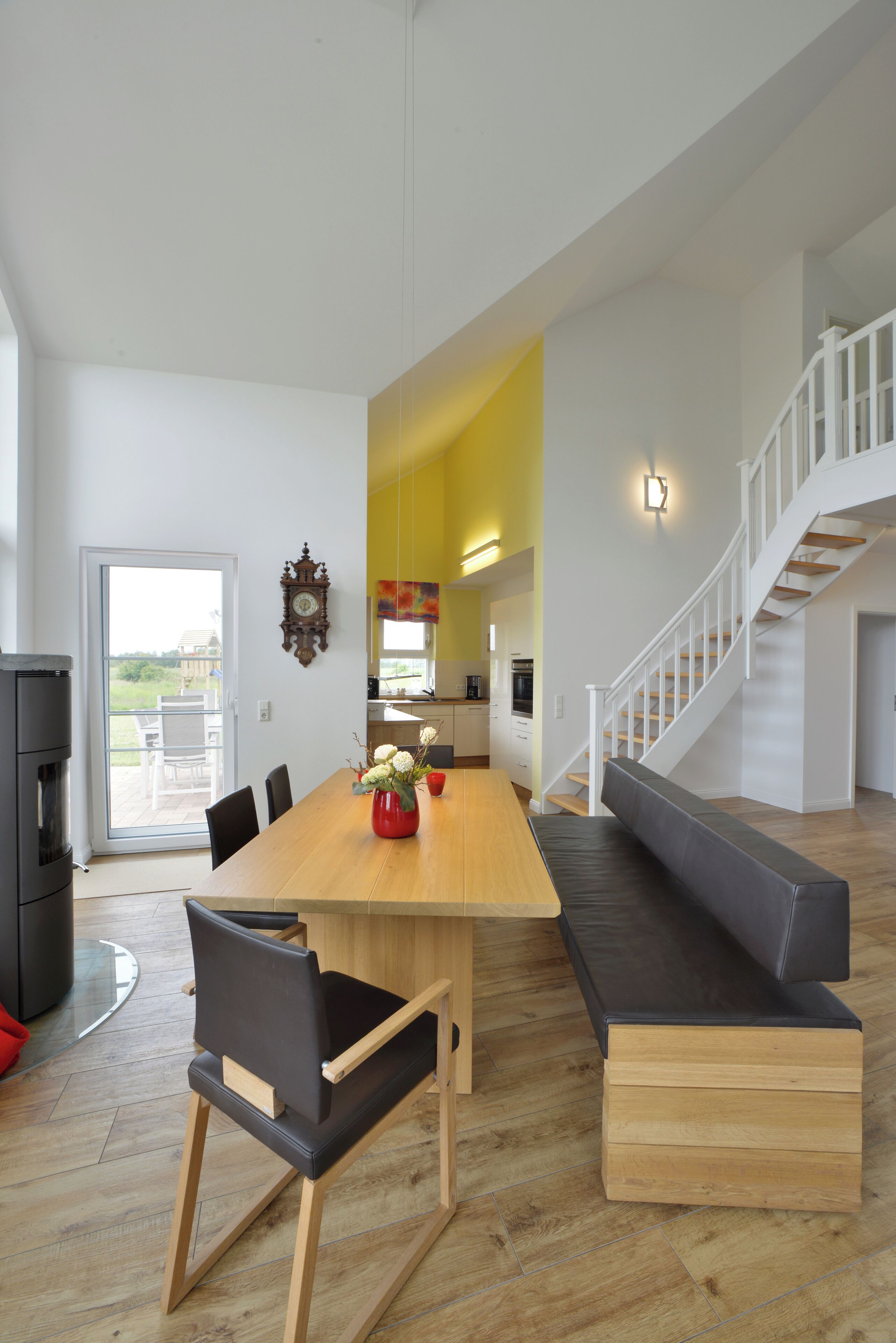 Een ruime woonkamer met een houten eettafel, een bank en een trap naar een verdieping erboven.