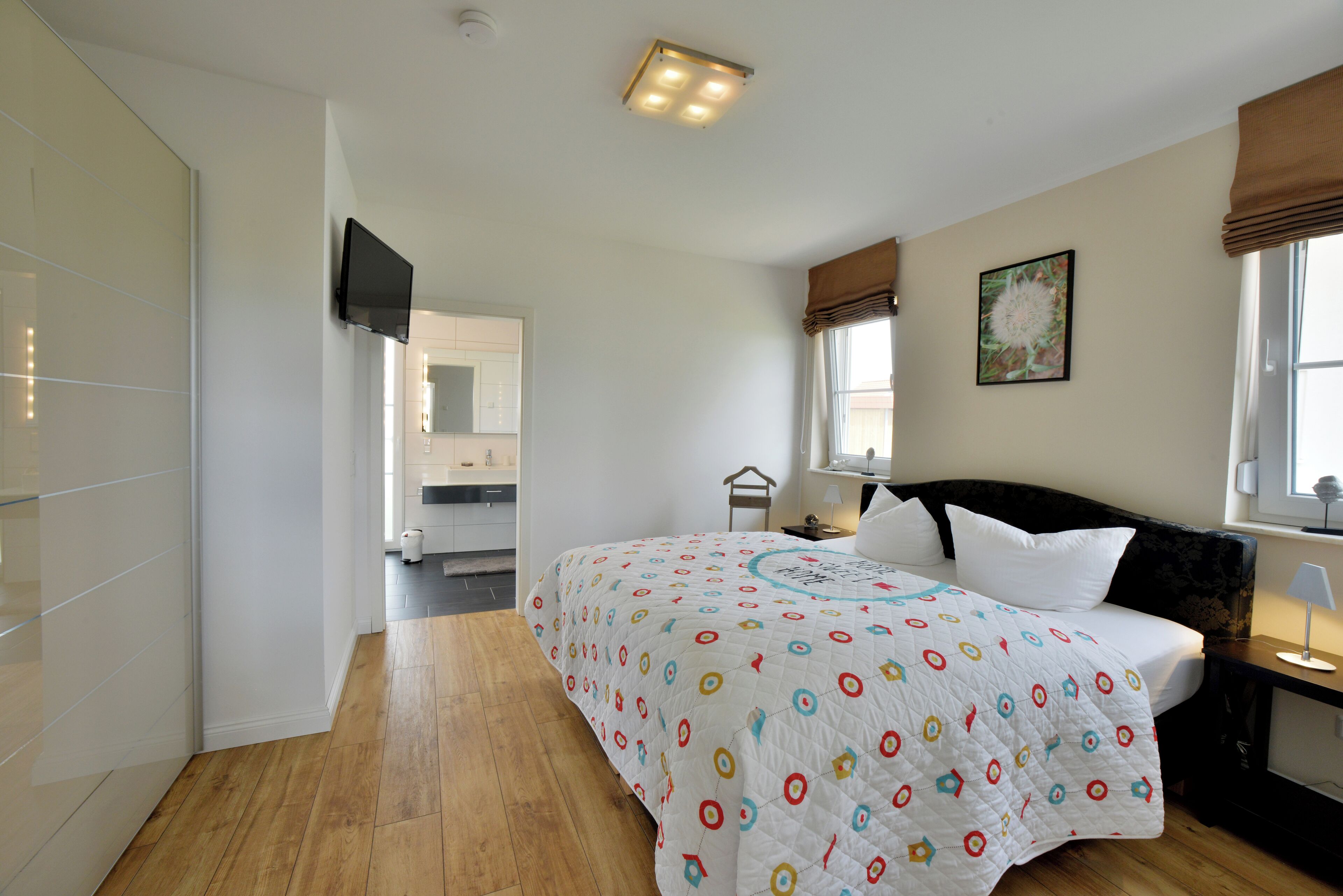 Een slaapkamer met een bed, een aan de muur bevestigde televisie, een raam met gordijnen en een deur naar een andere kamer.