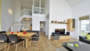 A spacious living area with a dining table, chairs, a sofa, and a TV. - Villa Kranich - High-quality vacation home in the middle of nature (Trent)