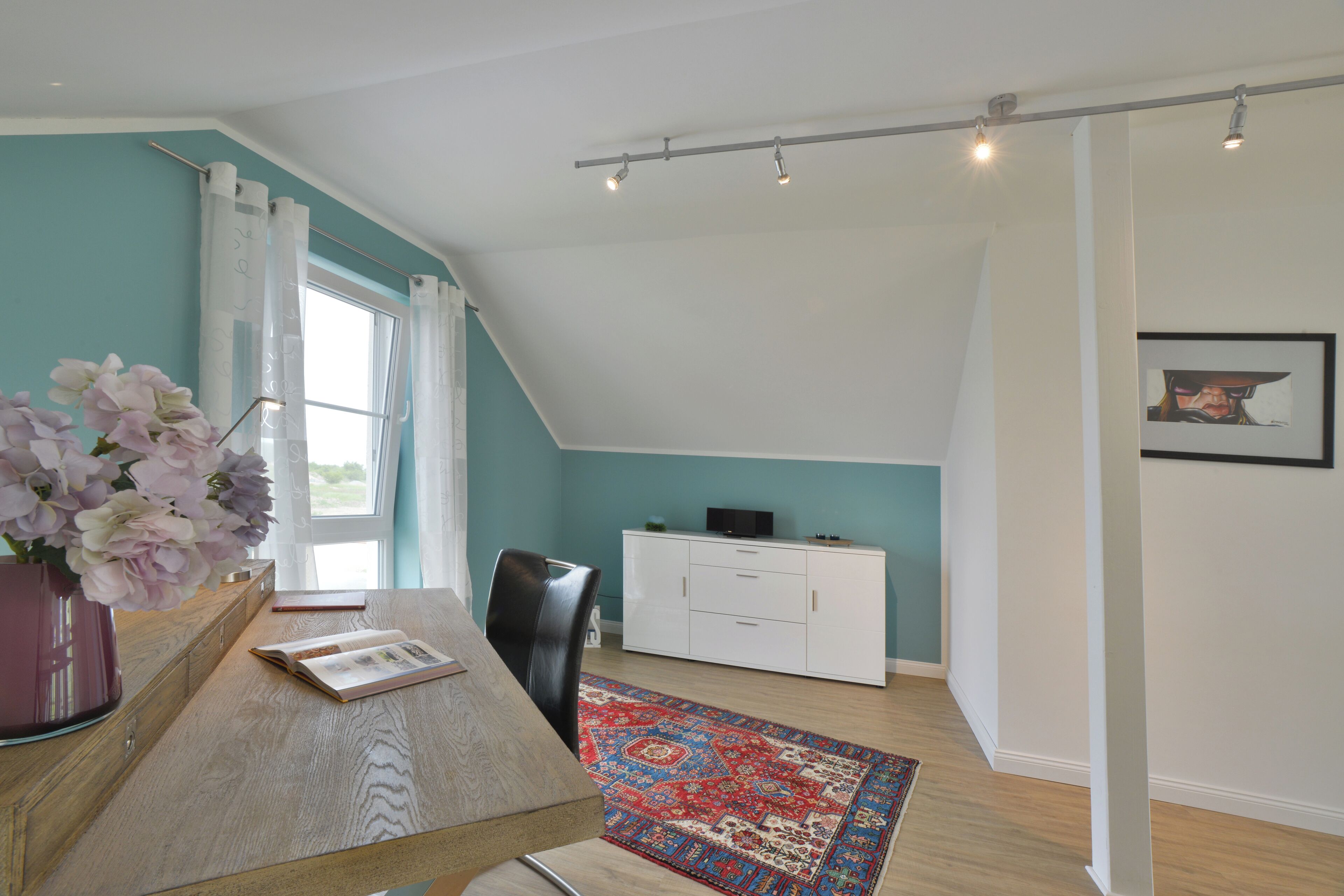 Een kamer met een eettafel, stoelen, een bloevas, een witte kast, een vloerkleed met rood- en blauw dessin, en een raam met gordijnen.