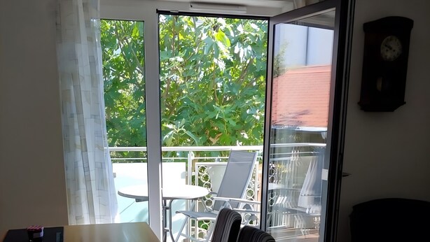 A room with a dining table, chairs, a sofa, and a view of an outdoor balcony with chairs and a table. - Dauth Apartment in the Heart of the Village (Kressbronn)