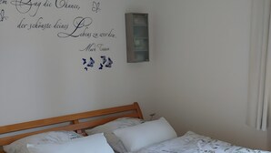 A neatly made bed with a floral bedspread, a wall with a motivational quote, and a small shelf. - Dauth Apartment in the Heart of the Village (Kressbronn)
