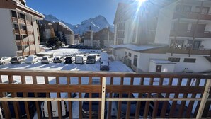 Un estacionamiento nevado con varios coches, una valla de madera y edificios al fondo.