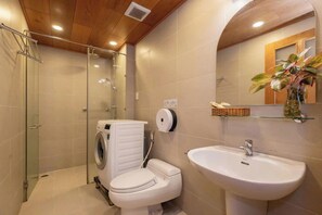 A modern bathroom with a glass shower enclosure, a built-in washing machine, and a pedestal sink. - Oasky Vung Tau - AnNam Village (Ho Chi Minh City)