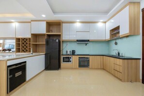 A modern kitchen with white cabinets, a black refrigerator, a microwave, and an oven. - Oasky Vung Tau - AnNam Village (Ho Chi Minh City)