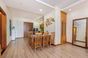 A dining area with wooden chairs and a table, a kitchen in the background, and a mirror on the wall. - Oasky Vung Tau - AnNam Village (Ho Chi Minh City)