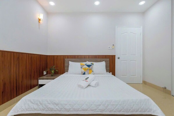 A hotel room with a bed, a wooden panel wall, a white door, and a wall-mounted light fixture. - Oasky Vung Tau - AnNam Village (Ho Chi Minh City)