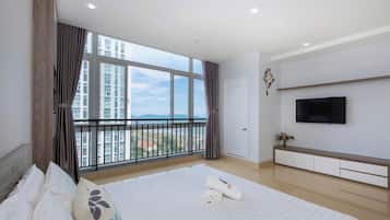 Quarto de hotel com uma cama grande, televisão fixada na parede e varanda com vista para edifícios e montanhas.