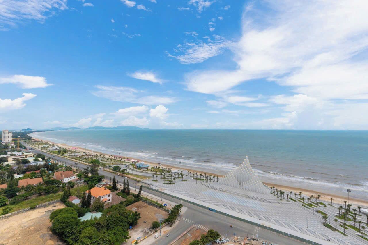 Paisagem costeira com praia, uma grande estrutura branca e uma estrada que leva à praia.