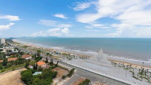A coastal cityscape with a beach, a large white structure, and a road leading to the beach. - Oasky Vung Tau - AnNam Village (Ho Chi Minh City)