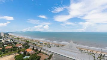 Paisagem costeira com praia, uma grande estrutura branca e uma estrada que leva à praia.