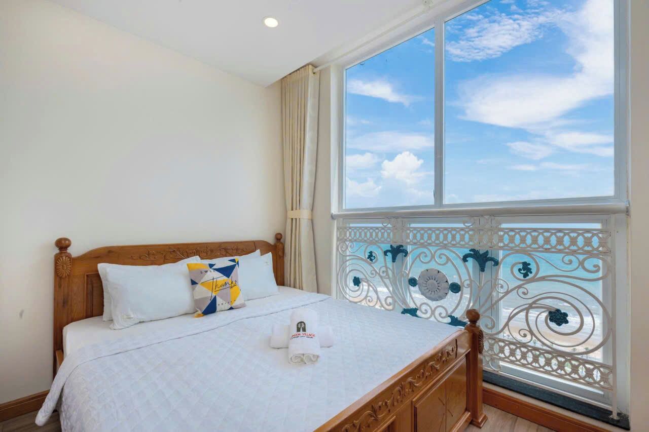 Quarto com uma janela grande, cama de madeira e varanda com grades de metal decorativas.