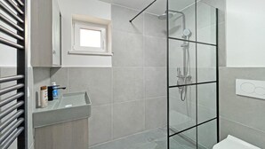 Une salle de bain moderne avec une douche à parois de verre, des toilettes blanches, un lavabo avec un distributeur de savon et un porte-serviettes.