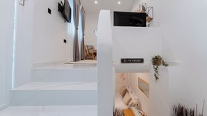 Une chambre d’hôtel moderne avec un panneau discret au-dessus de la porte, un téléviseur à écran plat fixé au mur, une chaise en bois et une petite table sur laquelle est posé un vase.