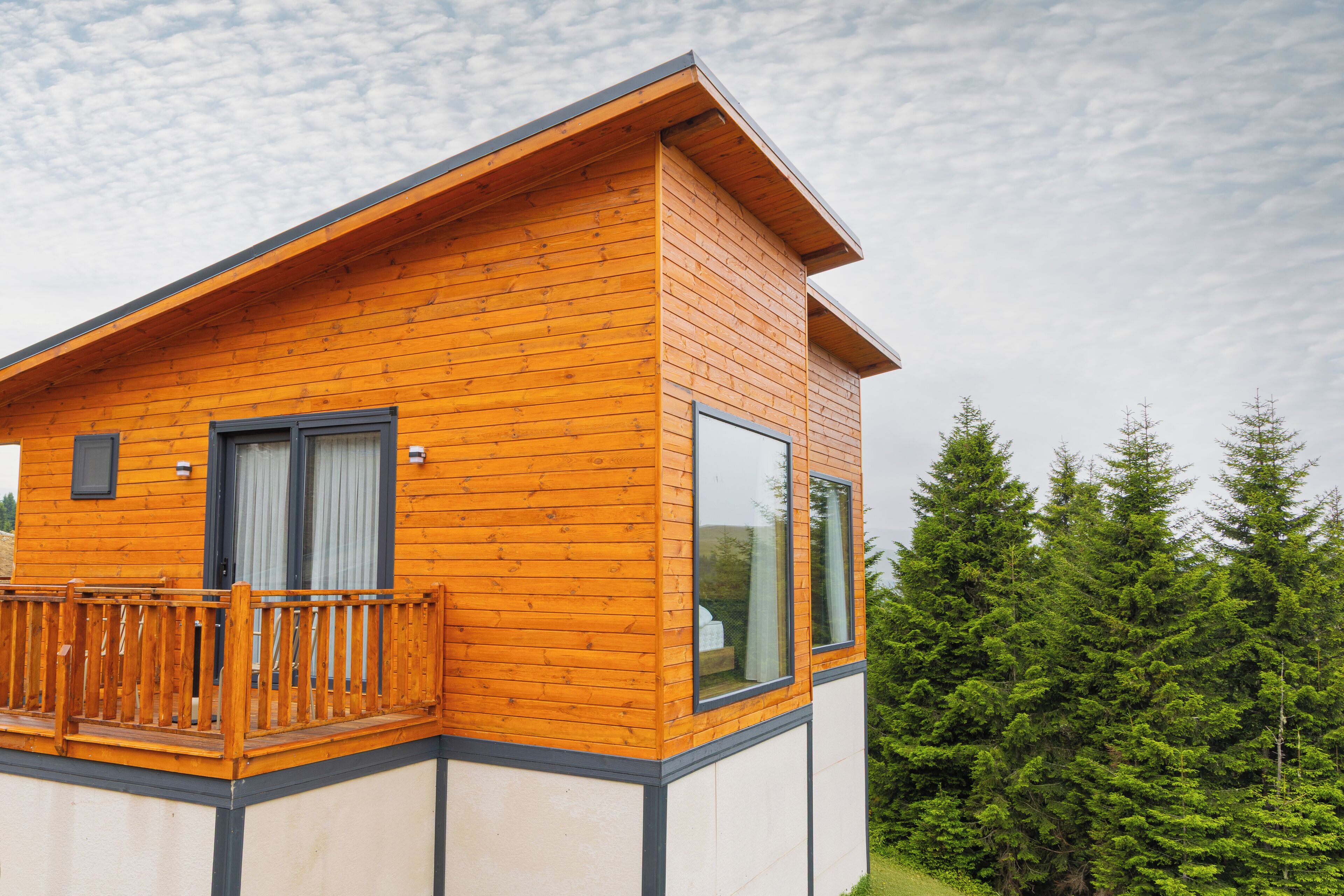 Un'accogliente baita moderna in legno con balcone, ampie finestre e vista sulla foresta.