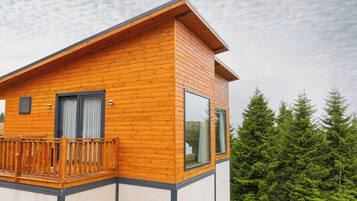 Un'accogliente baita moderna in legno con balcone, ampie finestre e vista sulla foresta.