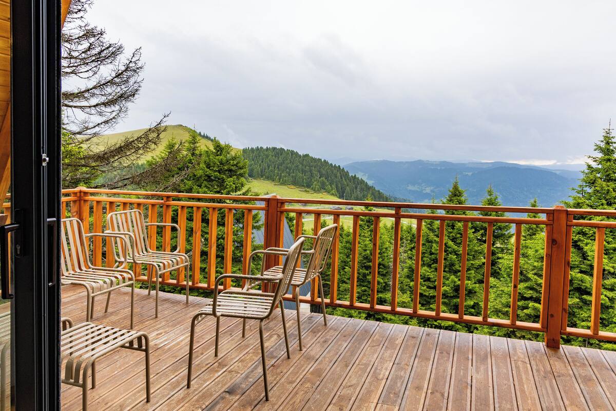 A wooden deck with four chairs and a view of a forested hillside.