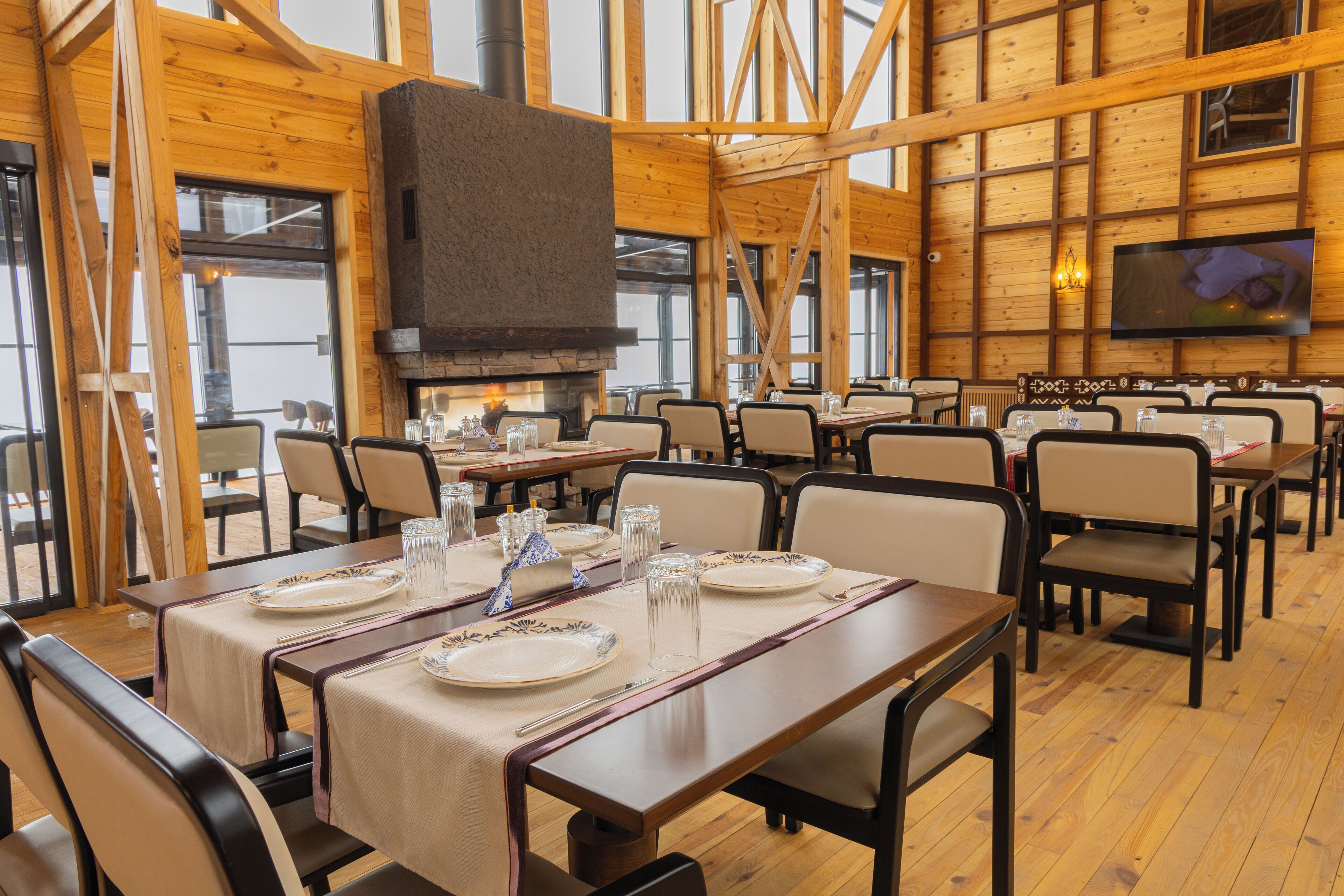 A restaurant with wooden walls and a fireplace. Tables are set with plates, glasses, and cutlery.