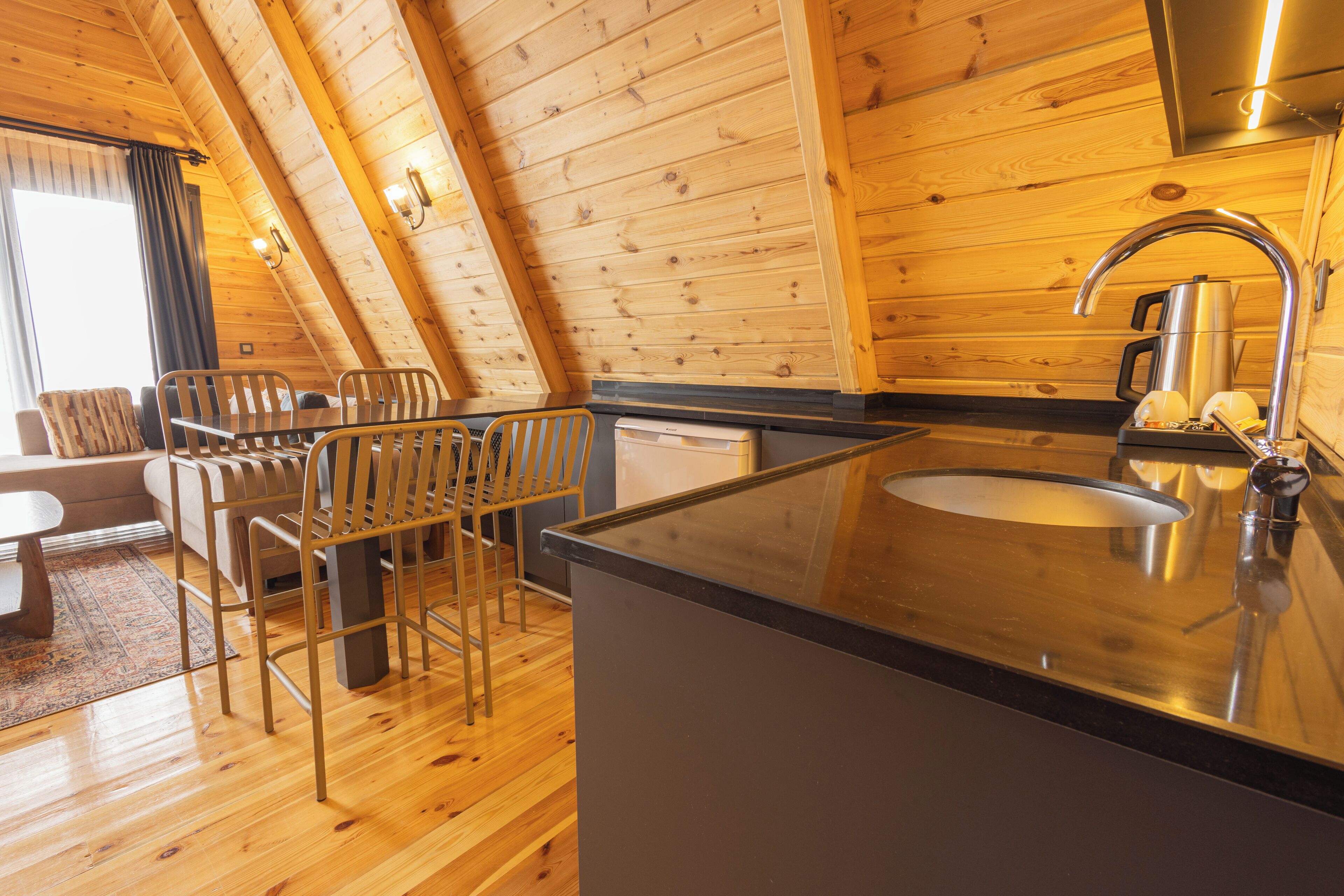 A cozy wooden cabin interior with a dining area, a kitchen with a sink, and a large window.