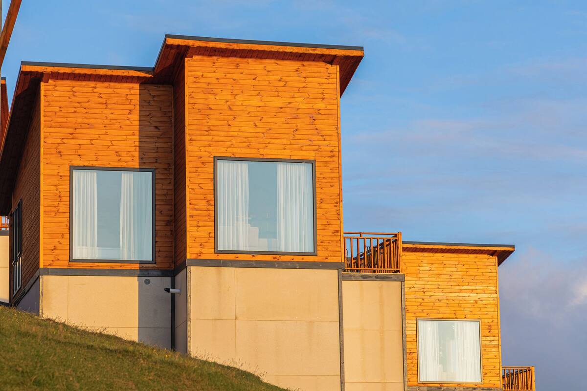 A modern wooden house with two visible windows and a small balcony.