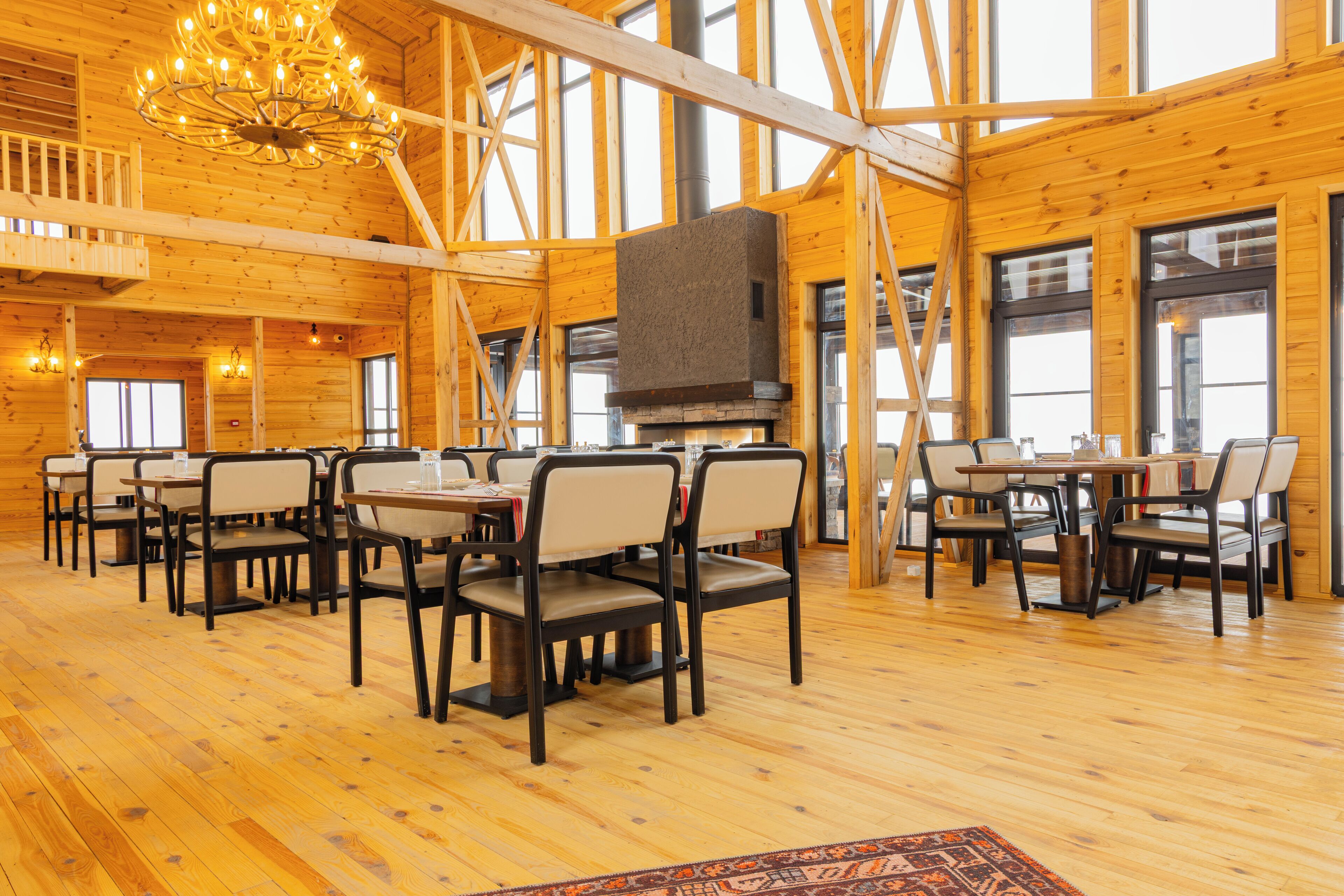 A spacious dining area with wooden floors and tables, a fireplace, and large windows.
