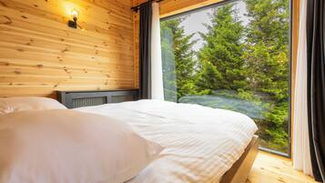 Un dormitorio de cabaña de madera con una cama grande, una ventana con cortinas y una lámpara fijada a la pared.