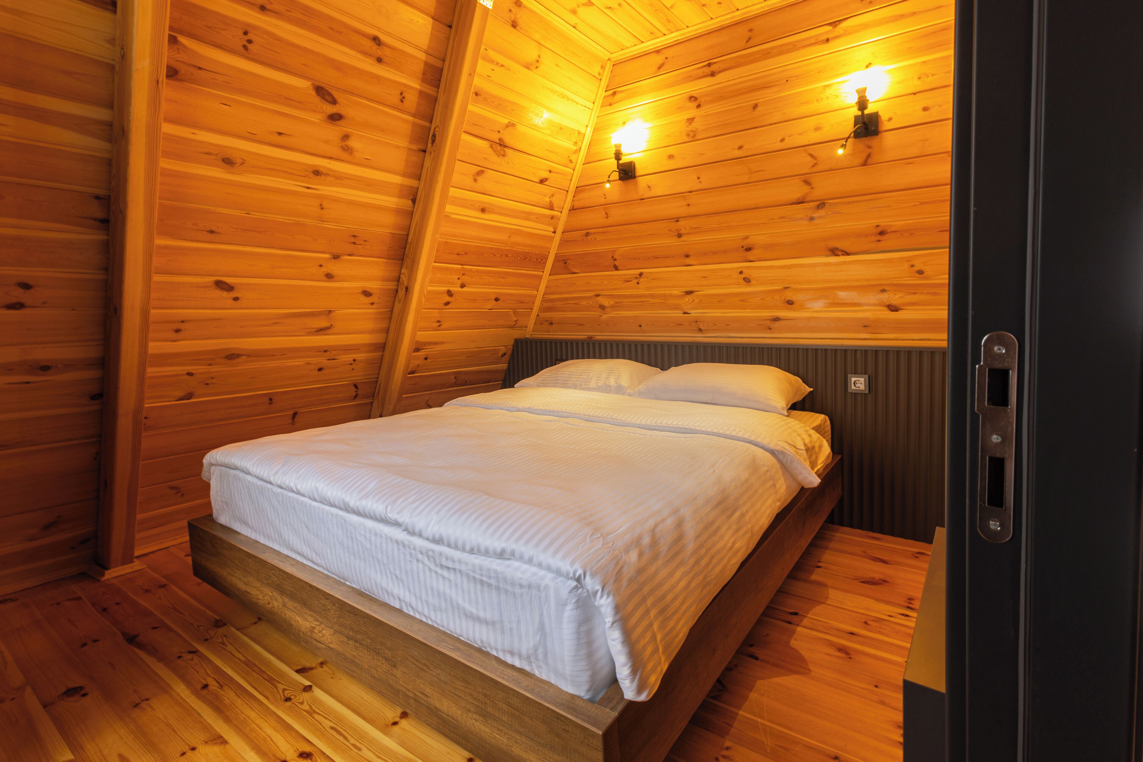 Una habitación con paneles de madera, una cama, dos luces fijadas a la pared y una puerta.