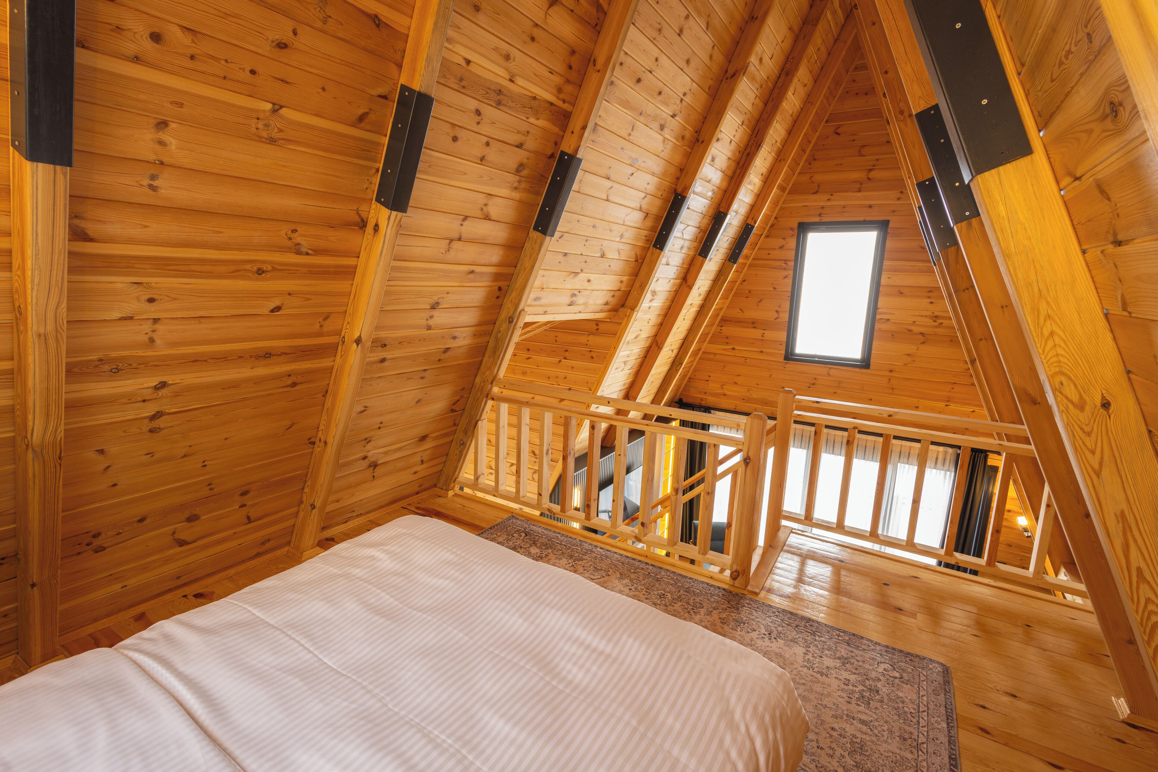 Una habitación de cabaña de madera con techo inclinado, una cama, un ventanal y una escalera.