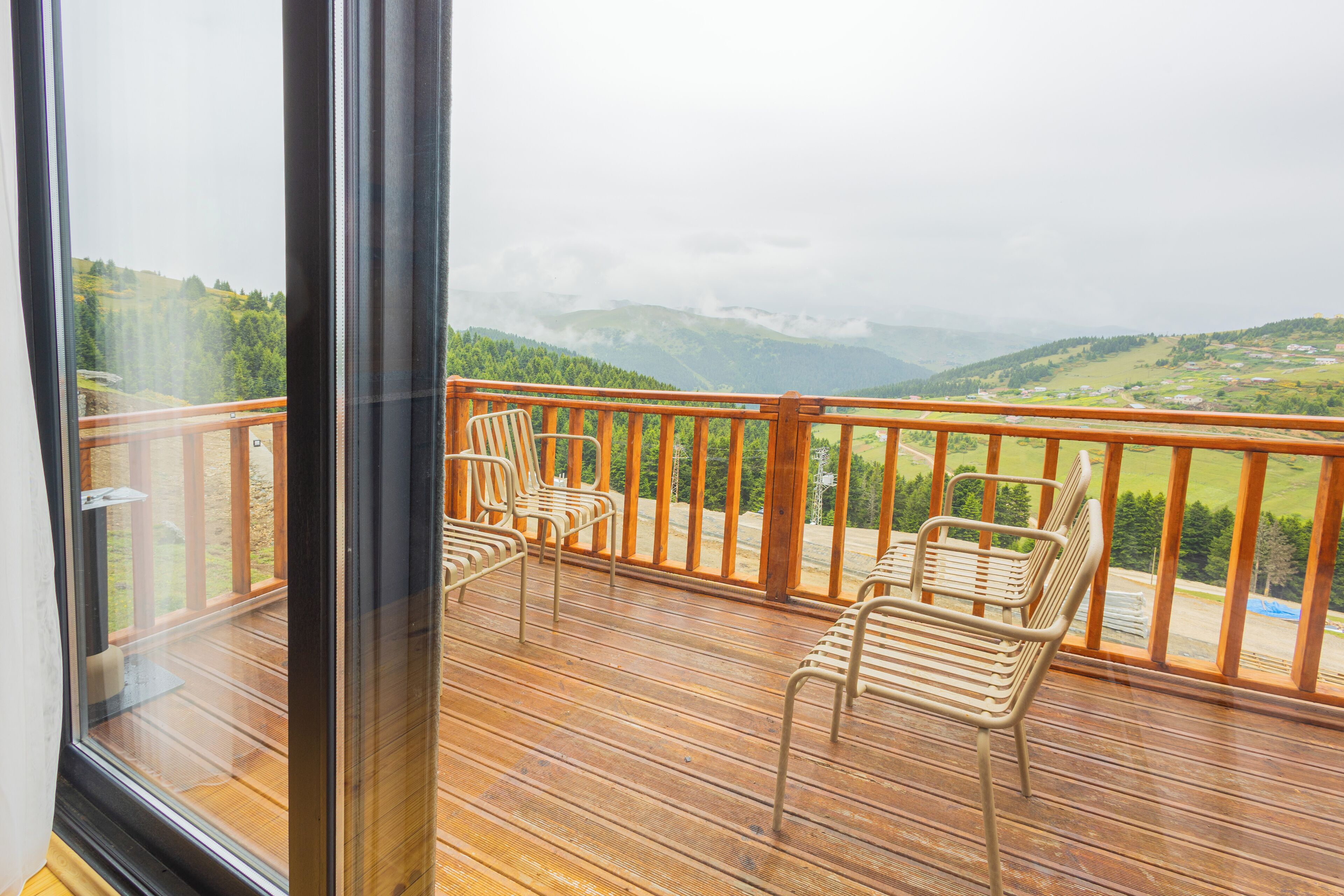 Un balcón con piso de madera y sillas de metal, con vistas a un paisaje montañoso.