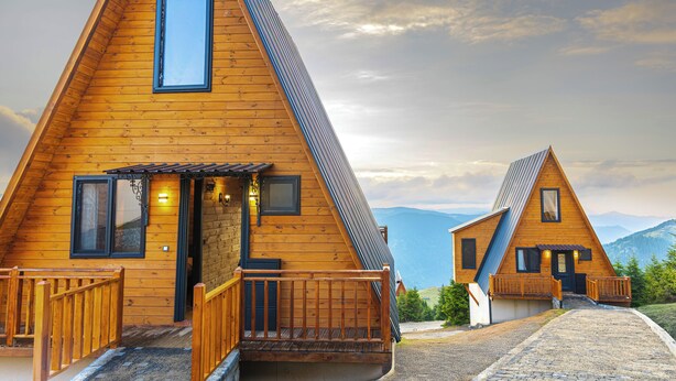 A wooden triangular house with a balcony and a door, set against a mountainous backdrop. - TİMİRA DAĞ EVLERİ (Dereli)
