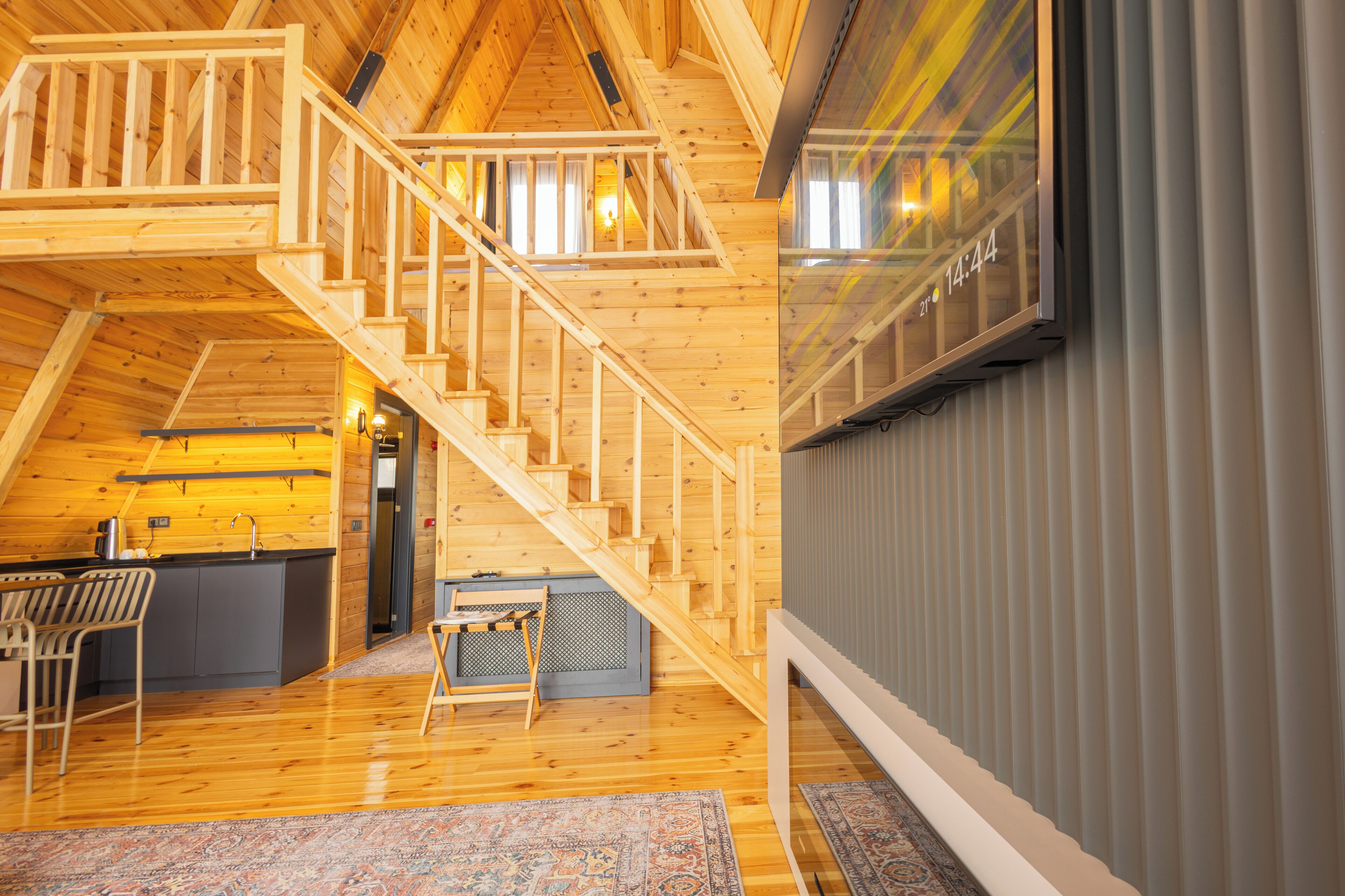 Un loft espacioso con escalera de madera, una zona de cocina y un amplio ventanal que muestra la hora.