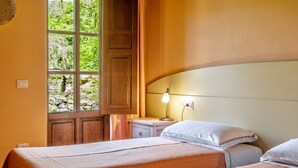 Ein Zimmer mit zwei Betten, einem Fenster mit Blick auf Grünflächen, einem Nachttisch mit Lampe und Holzvertäfelung an den Wänden.